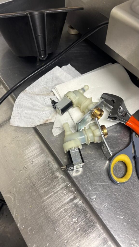 The old, worn water inlet valve assembly removed for replacement, shown next to service tools.